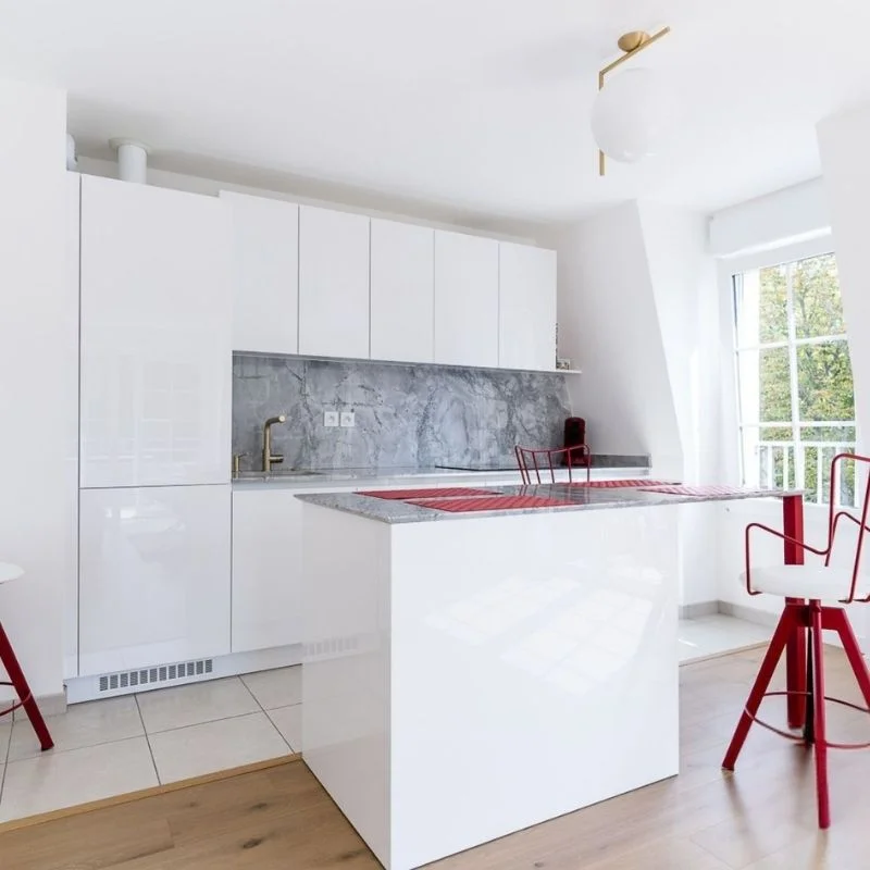 Cuisine blanche laquée avec crédence en marbre gris, îlot central et chaises rouges