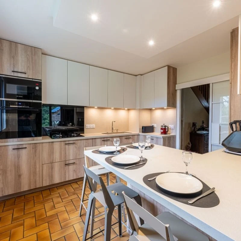Cuisine en U avec façades bois et blanches, îlot central dressé et sol en carrelage terre cuite