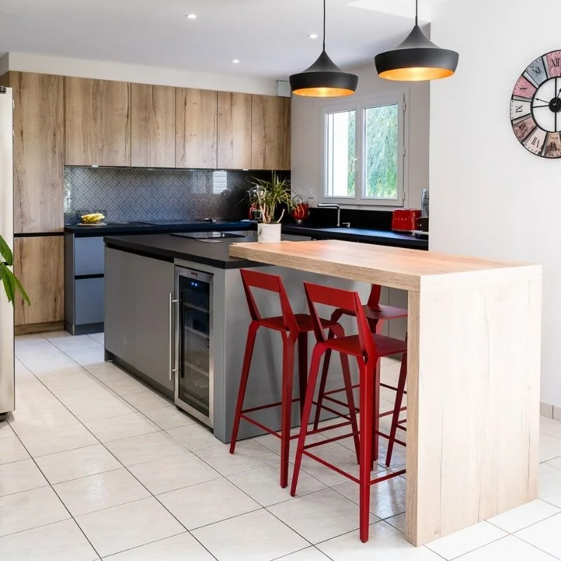 Cuisine ouverte avec îlot central en bois clair, façades grises et chaises hautes rouges