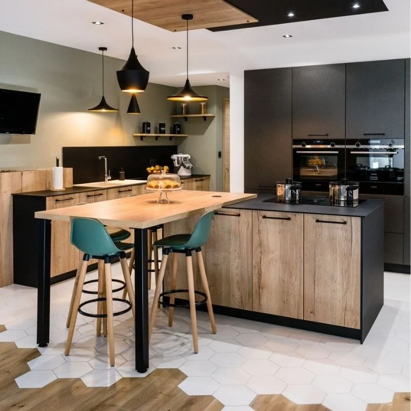 Cuisine noire et bois avec îlot central prolongé en table et chaises vertes, et carrelage hexagonal, réalisation So!Cozi