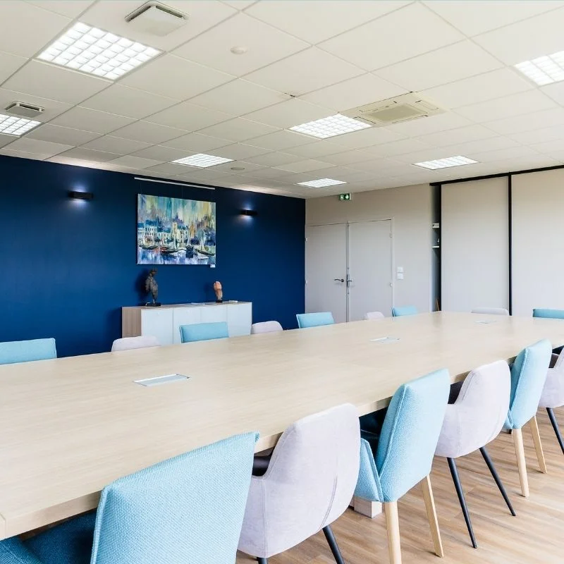 Salle de réunion avec grande table bois et mur bleu marine, aménagement So!cozi