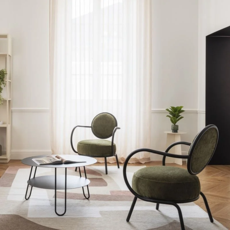 Salon moderne avec deux fauteuils Joséphine de Resistub, ronds rembourrés verts et une table basse en métal noir sur laquelle est posé un livre.