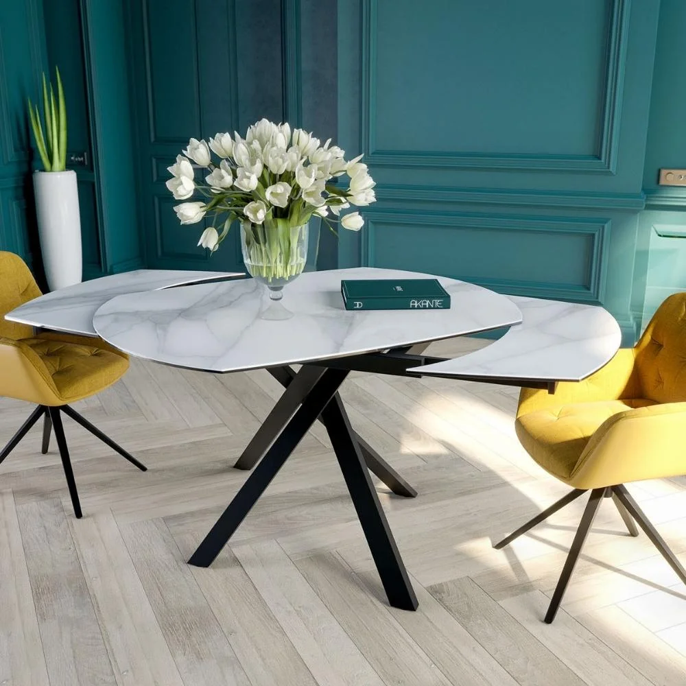 Table ronde Akante moderne en marbre blanc avec pieds noirs et deux chaises au revêtement jaune, dans une pièce lumineuse.