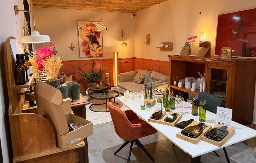 Intérieur du magasin So!Cozi chaleureux avec mobilier en bois, vases décoratifs, bouteilles, plantes et éclairage chaleureux.