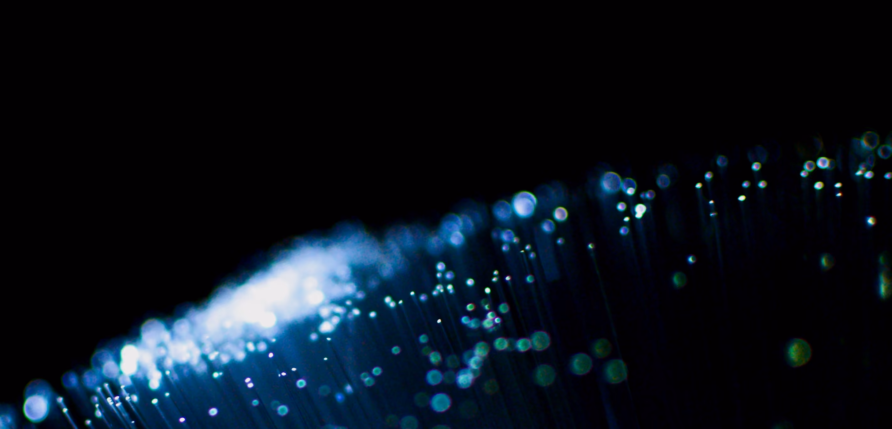 Close-up of glowing fiber optic cables with blue light against a dark background.