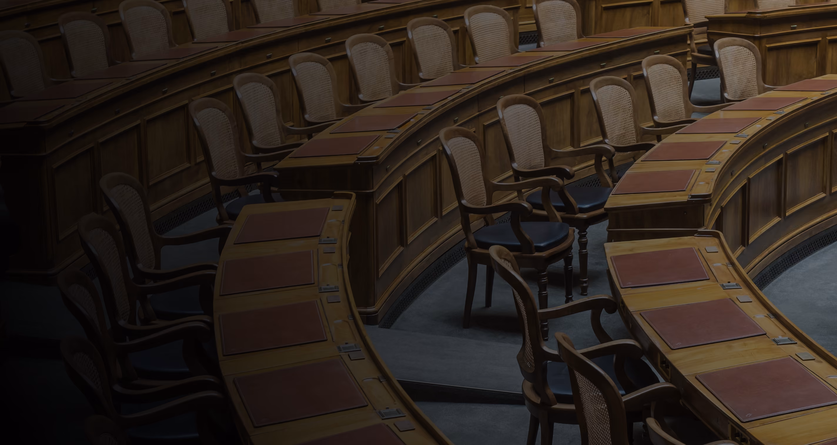 Empty curved wooden desks and chairs in a formal meeting or legislative chamber.