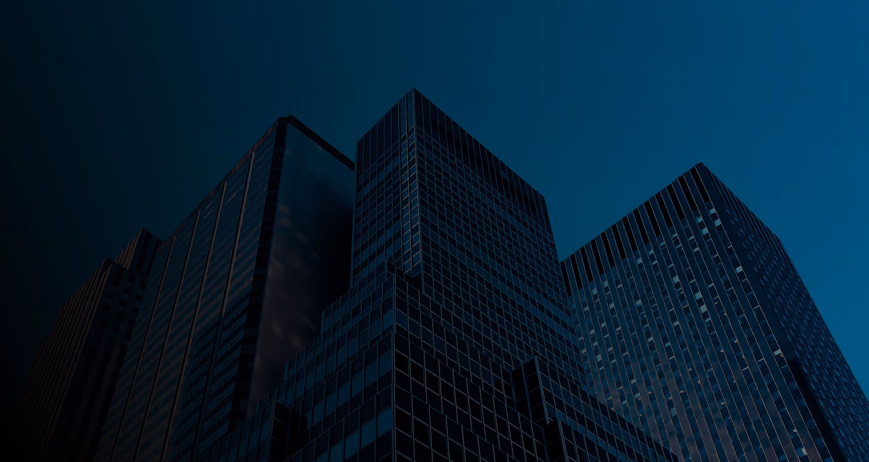 Low-angle view of modern glass skyscrapers against a dark blue evening sky.