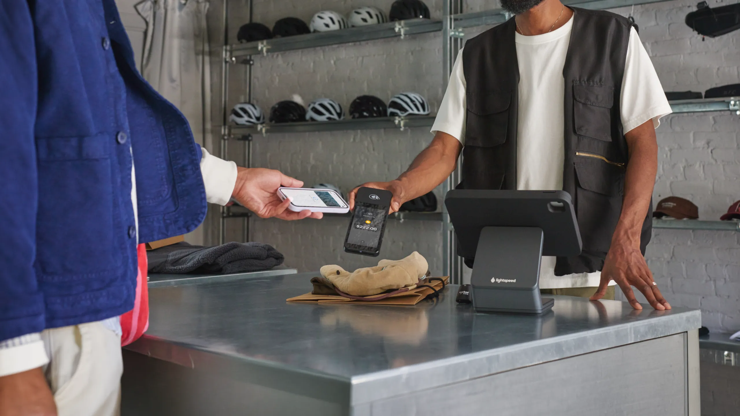 A customer making a contactless payment using a smartphone and a card reader at a retail counter.