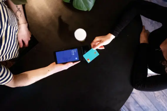 Two people at a table, one holding a smartphone, the other paying with a credit card.