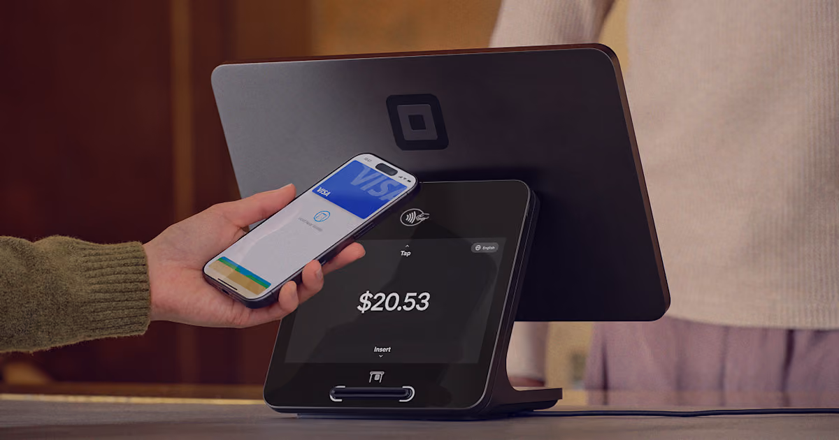 Person holds smartphone with Visa card app close to a modern payment terminal showing $20.53.