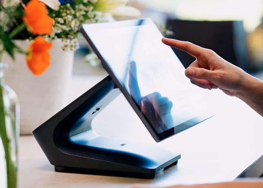 Hand interacting with a touchscreen point-of-sale system on a modern black stand.