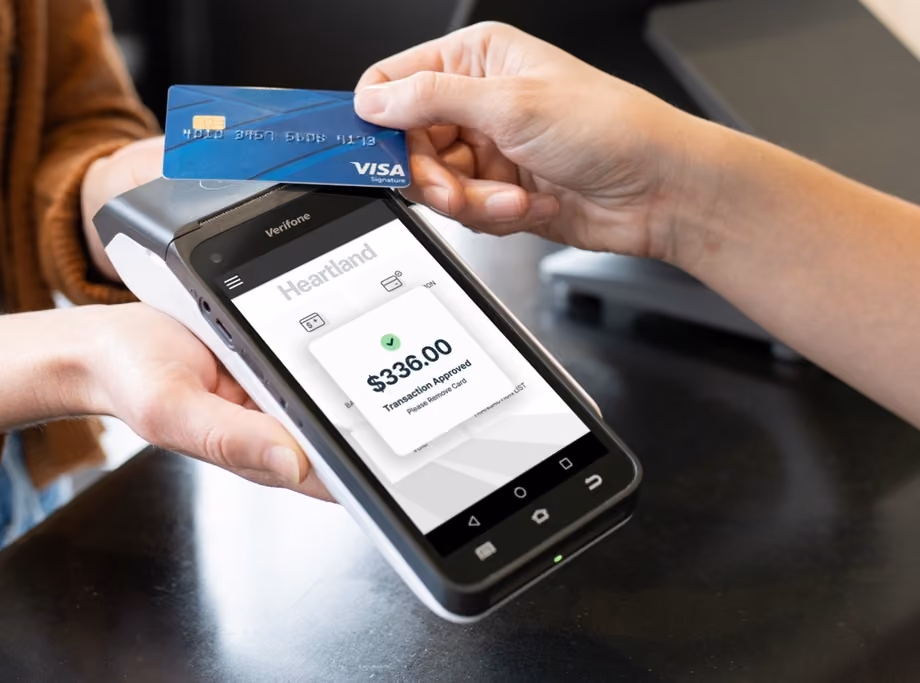 Person holding a Verifone card reader showing approved $336 transaction while another taps a Visa card.
