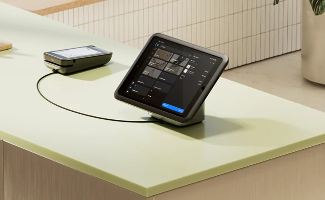 Modern point-of-sale tablet and card reader connected by cable on a light green countertop.