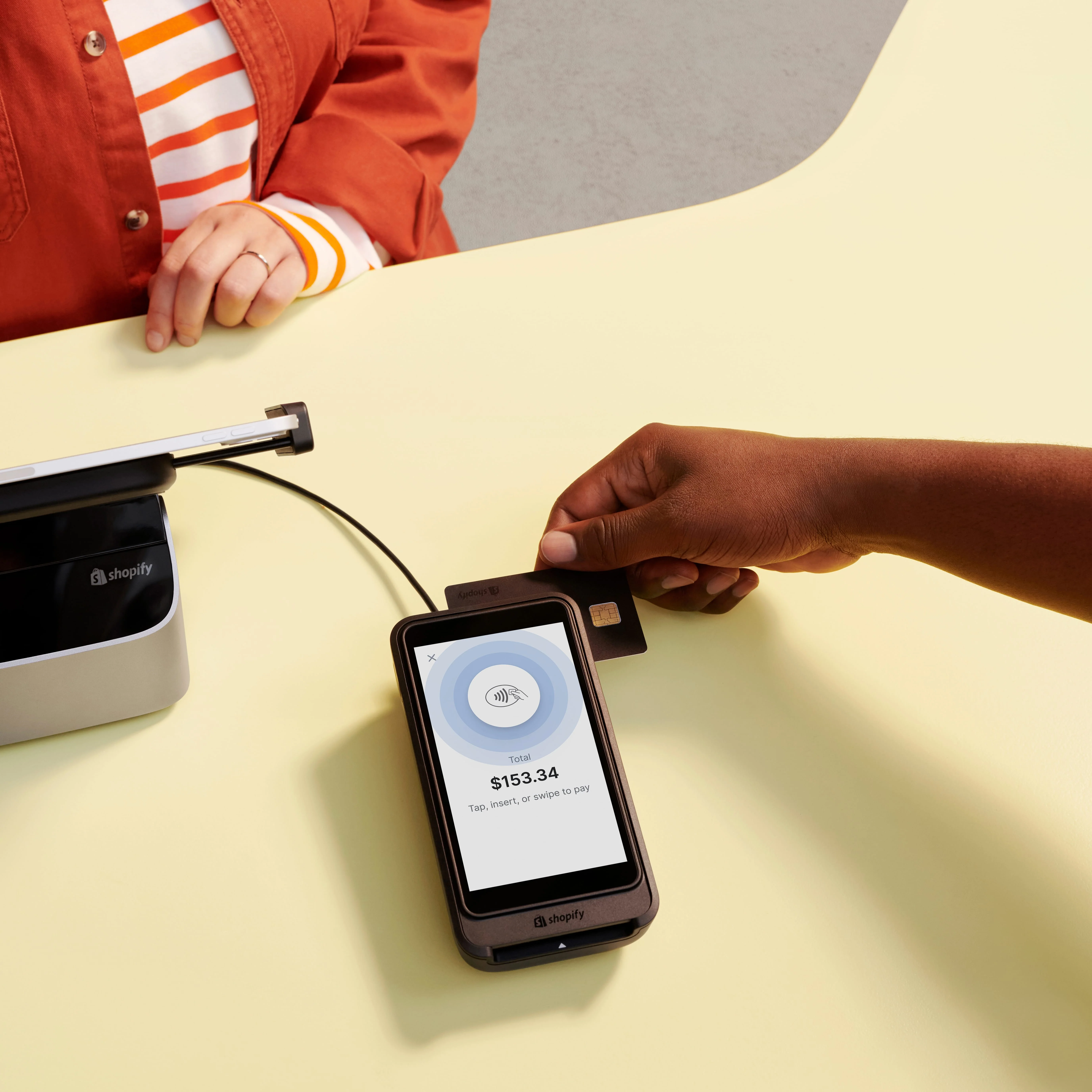 Person swiping a card on a Shopify card reader showing $153.34 payment total on screen.