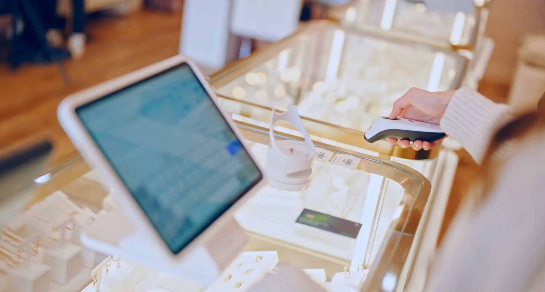 Person using a handheld card reader over a glass jewelry display case with a tablet nearby.