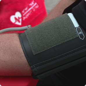 Person's arm wearing a blood pressure cuff with tubing attached for measurement.