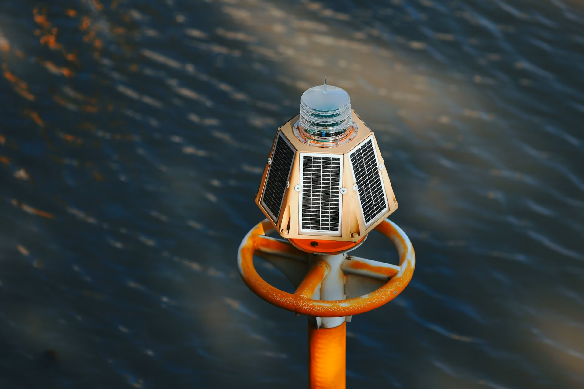 Close-up of a small solar-powered navigation or warning light mounted on a rusty yellow post above water.