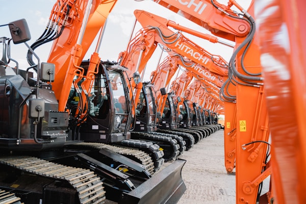 Eine Reihe von Hitachi Baggern, die für den Einsatz auf einer Baustelle bereitstehen. Diese modernen und leistungsstarken Maschinen sind ideal für eine Vielzahl von Bauprojekten und zeigen die Effizienz und Zuverlässigkeit von Hitachi Baumaschinen