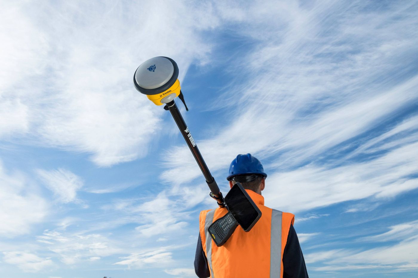Surveyor carrying a GNSS rover pole under a blue sky