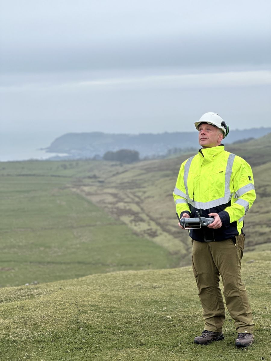 Drone pilot in a hi-vis jacket flying a survey drone above the coast