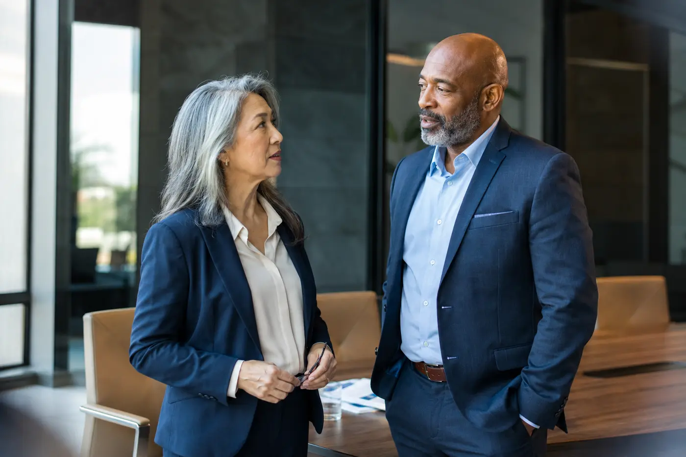 Two late-career corporate executives in conversation in a modern office