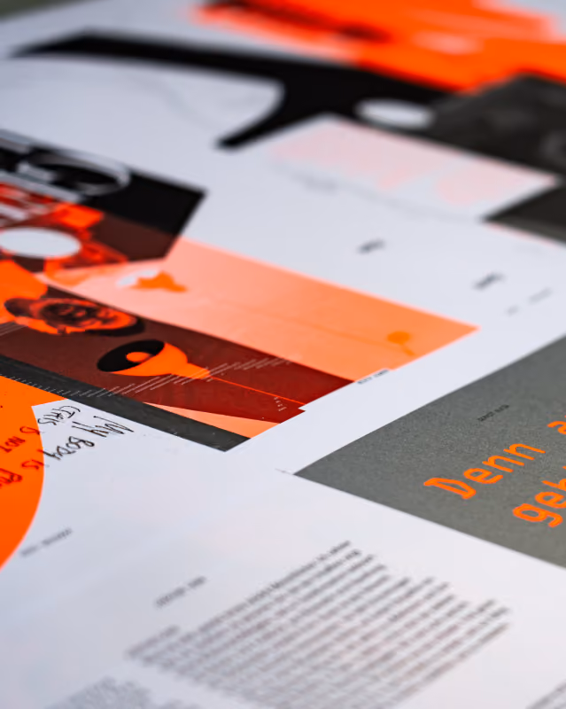 Nahaufnahme von Buchseiten und Grafiken mit Orange- und Schwarztönen, verstreut auf einem Tisch.