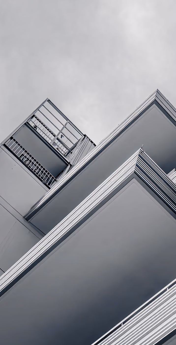 Low-angle view of modern building with metal railings and sharp architectural lines against a gray sky.