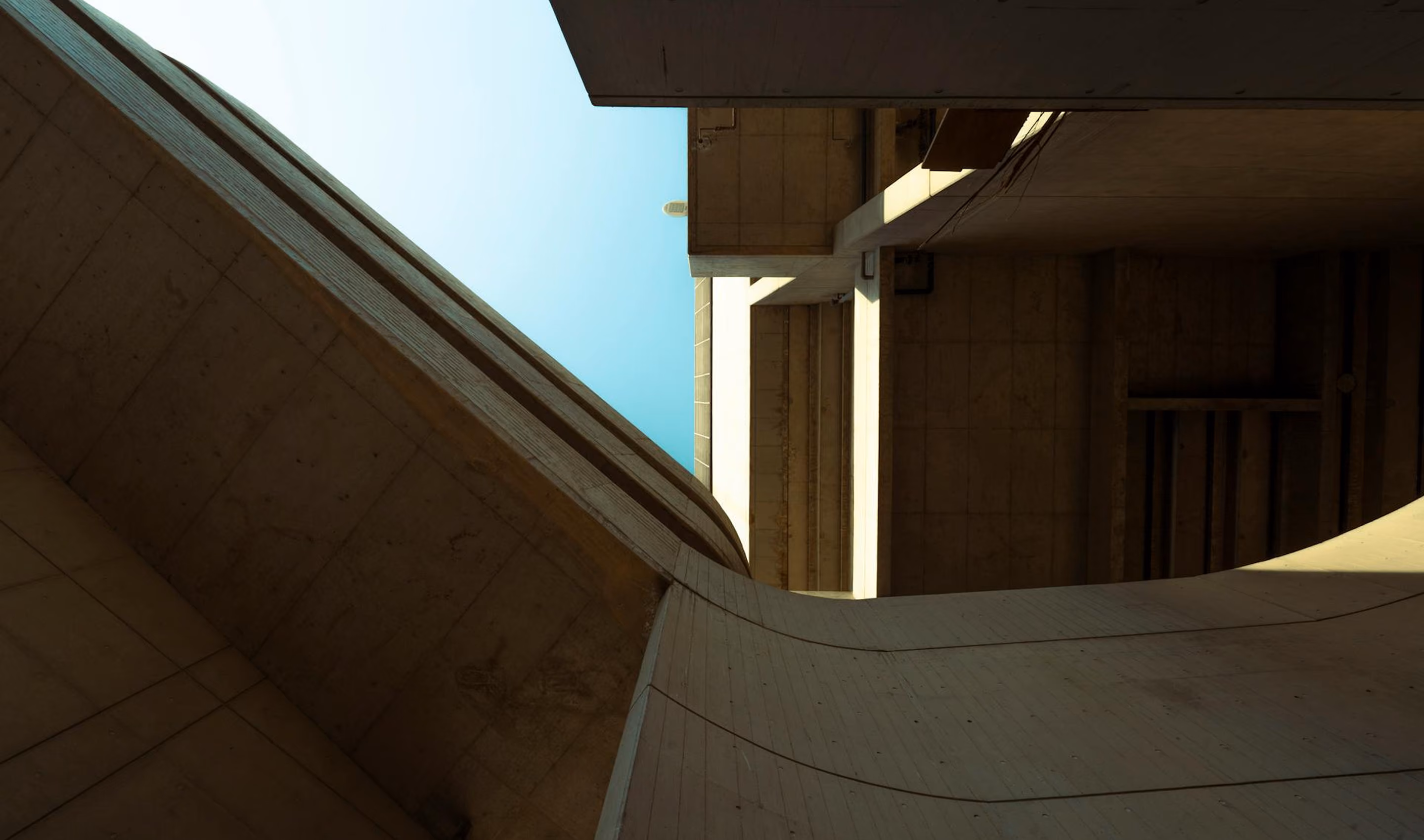 View looking up at modern concrete building structures against a clear blue sky.