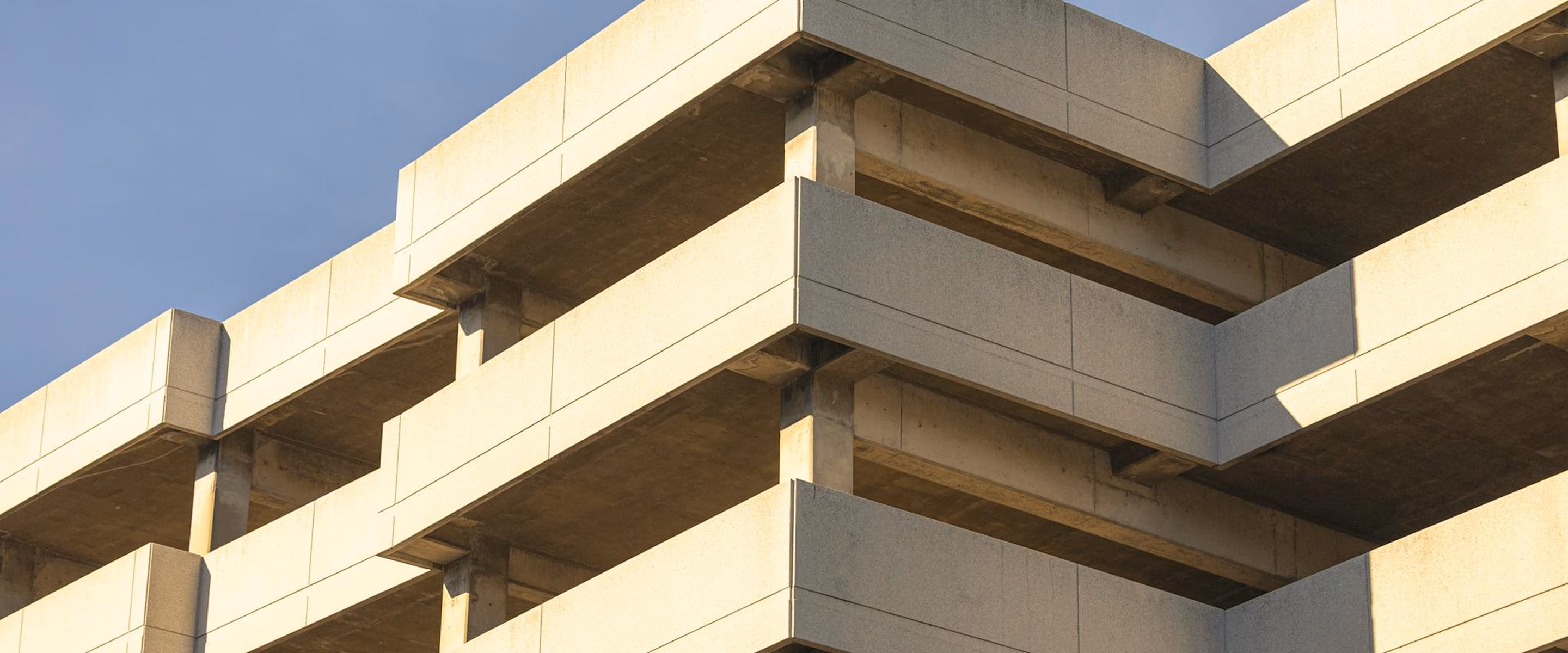 Close-up of a concrete building corner showing geometric, layered balconies under a clear sky.