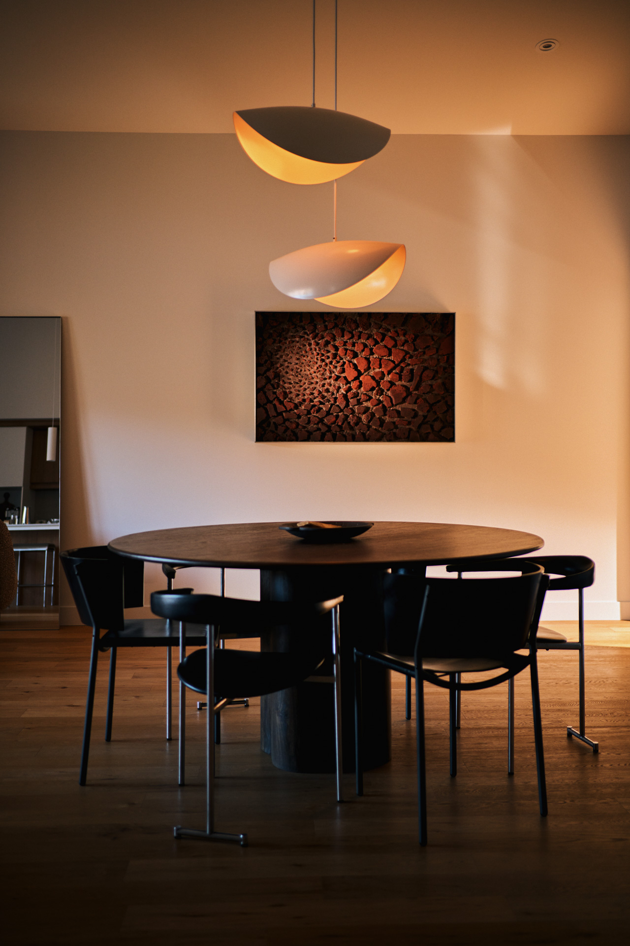 Dining area in a Rive Lac Tremblant condo with round wood table, sculptural pendant lights and textured artwork