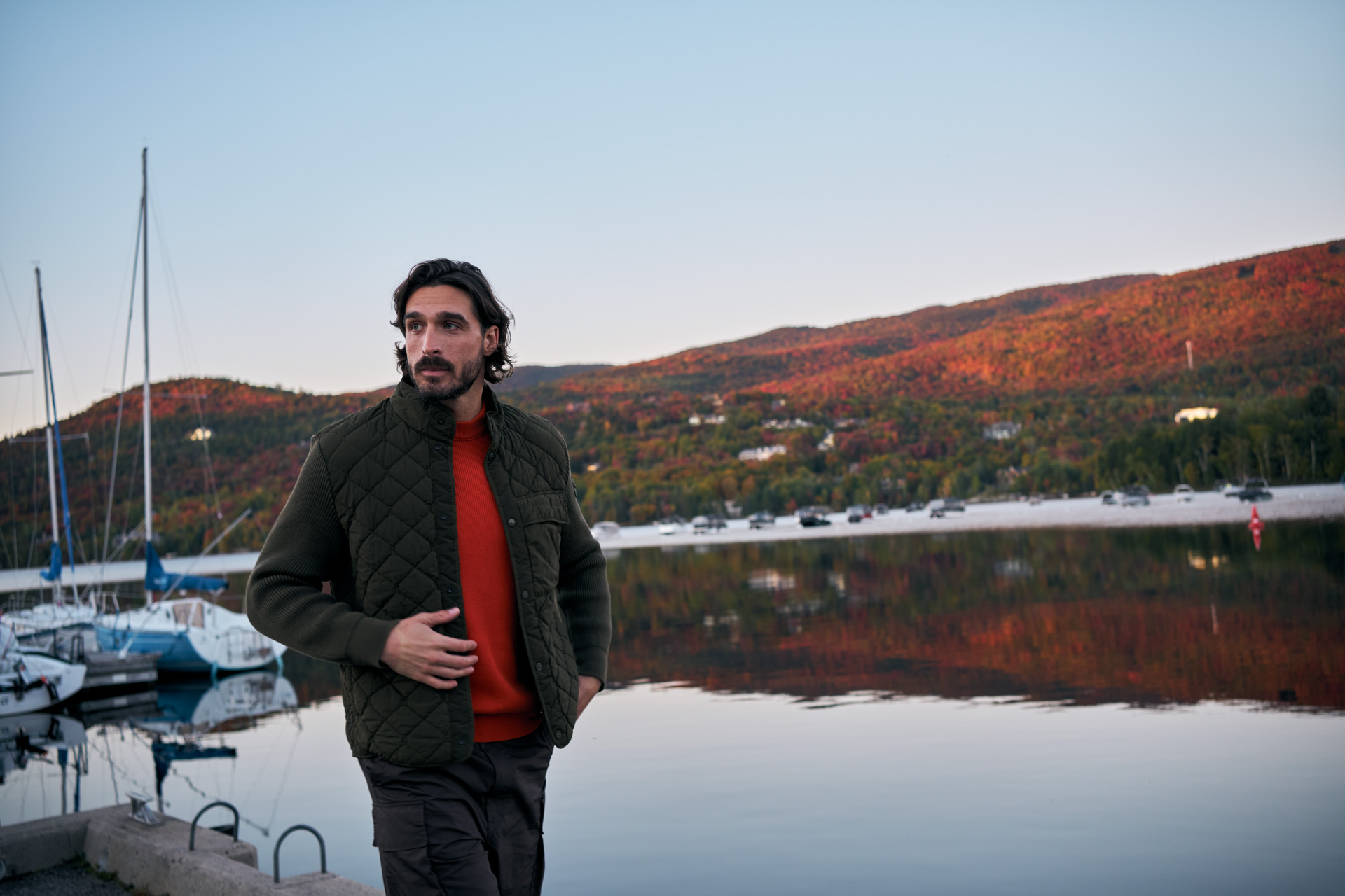 Man walking along a marina on Lake Tremblant with autumn mountains reflected in the water