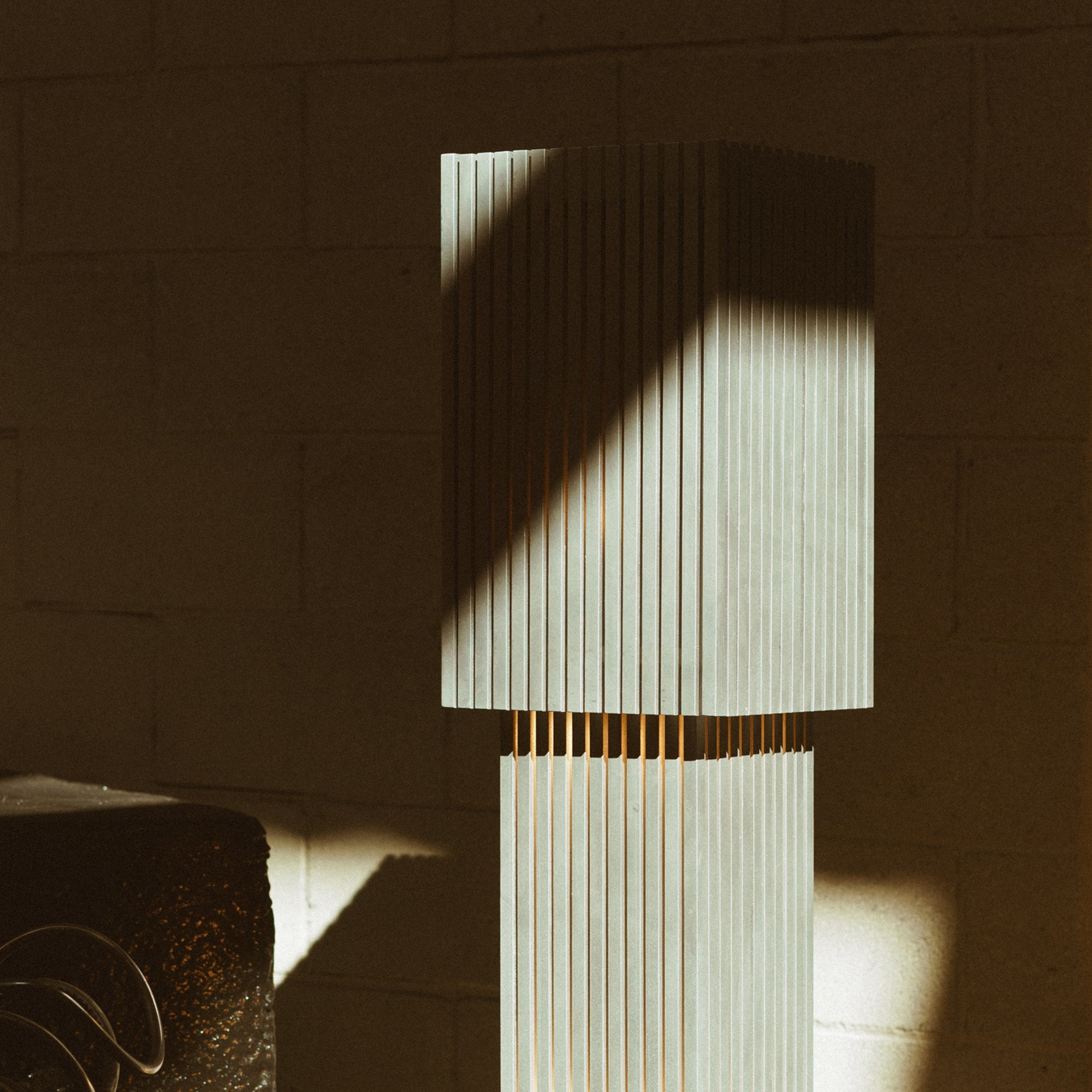 Lampadaire à lattes de bois clair éclairé par un rayon de soleil contre un mur de blocs