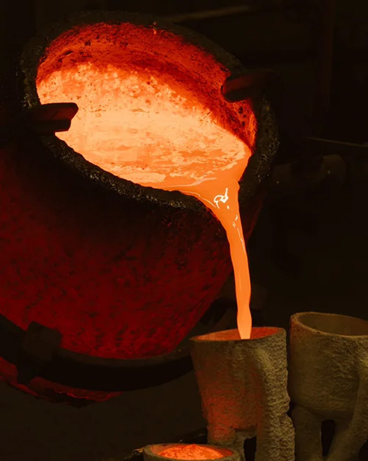 Métal en fusion versé d'un creuset dans des moules dans une fonderie artisanale