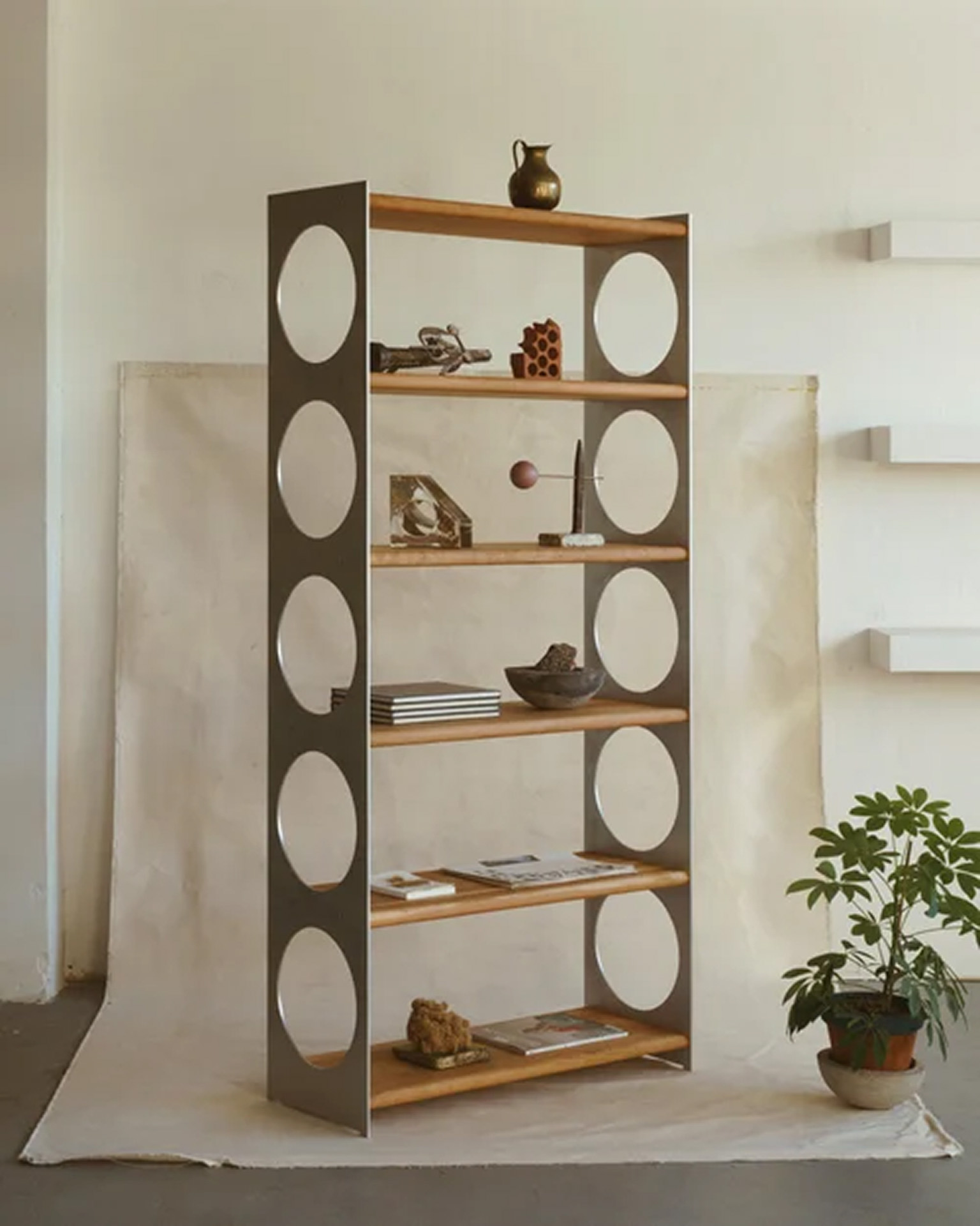 Étagère en acier brossé et chêne aux découpes circulaires garnie de céramiques et de livres