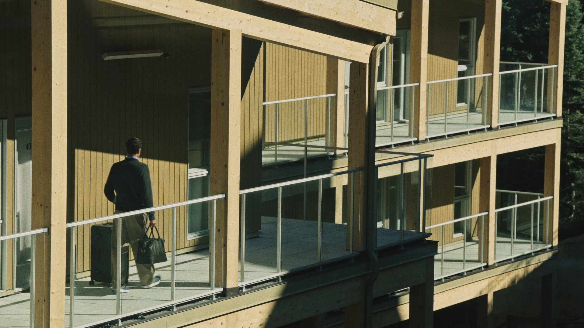 Guest arriving with luggage along the wood-clad exterior walkway at Rive Lac Tremblant