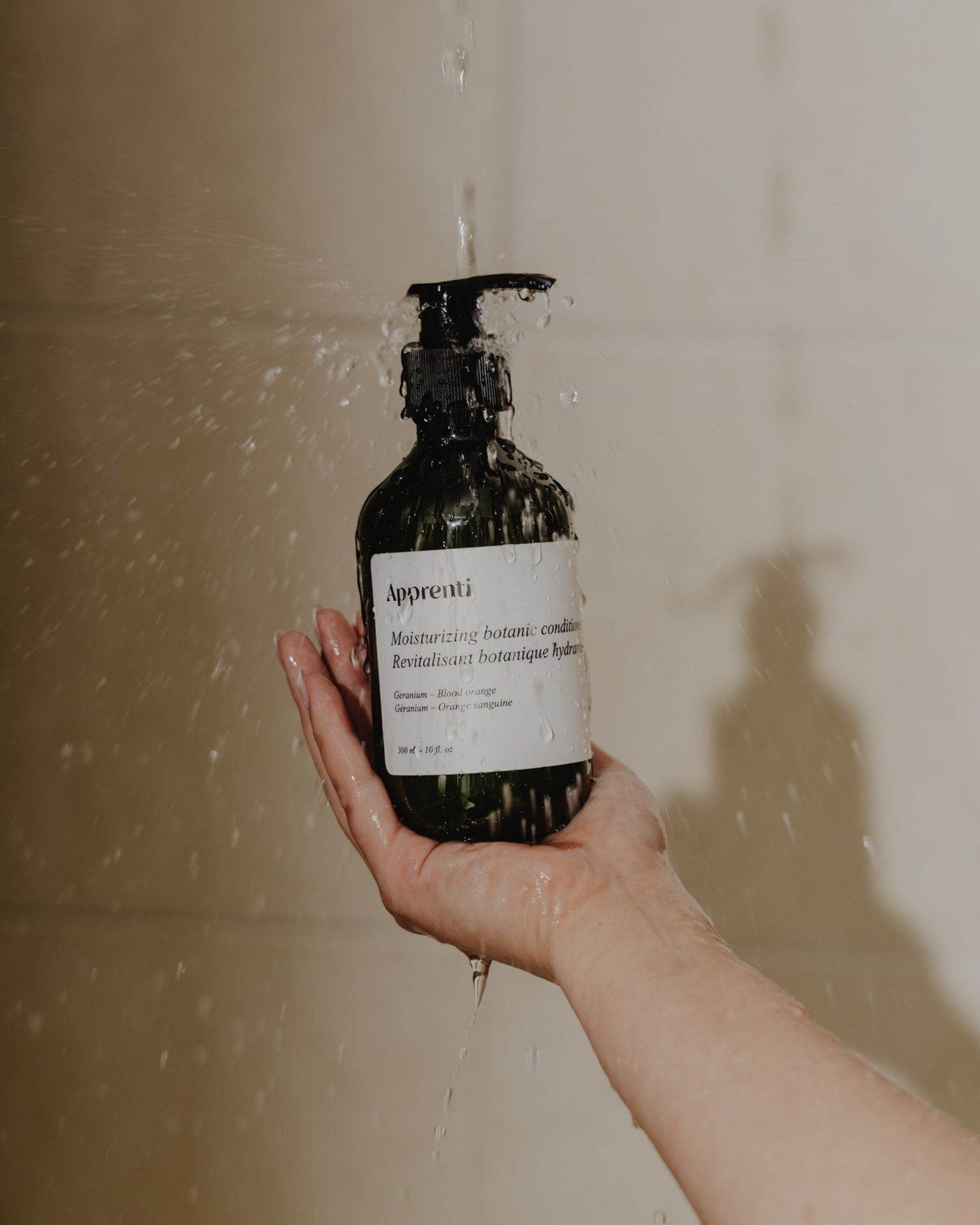 Apprenti botanical conditioner bottle held under a running shower