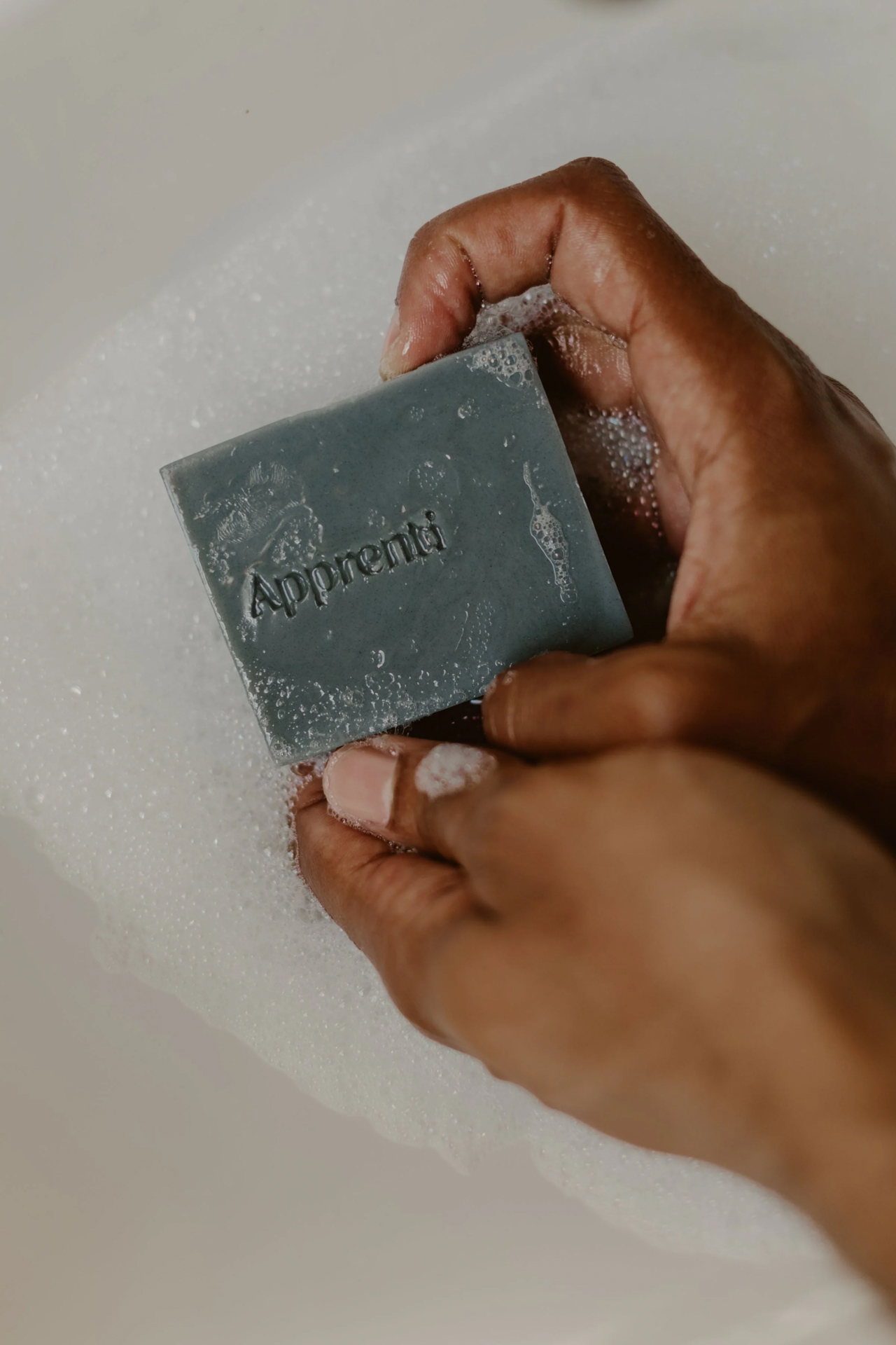 Hands lathering a grey Apprenti handmade soap bar