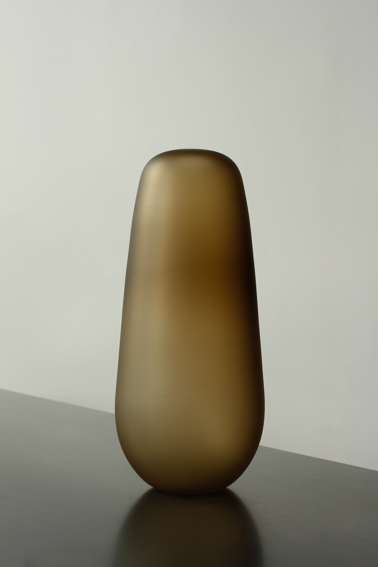 Smoky amber frosted glass vase by Verre d'Onge on a dark tabletop