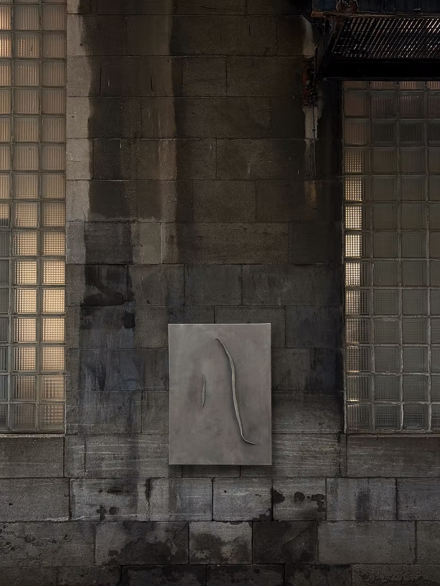 Grey textile artwork by Felix Paquet mounted on a stone wall between glass block windows