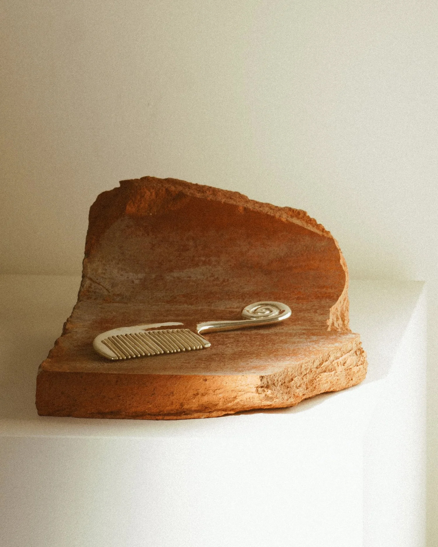 Silver spiral comb by Jeremy Le Chatelier resting on a terracotta stone fragment