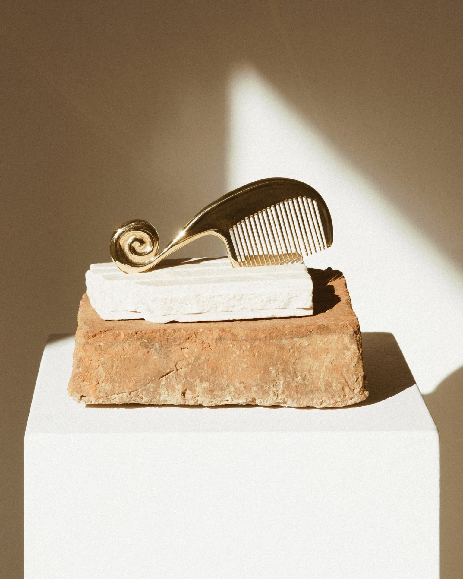 Gold spiral comb by Jeremy Le Chatelier displayed on brick and stone atop a white plinth