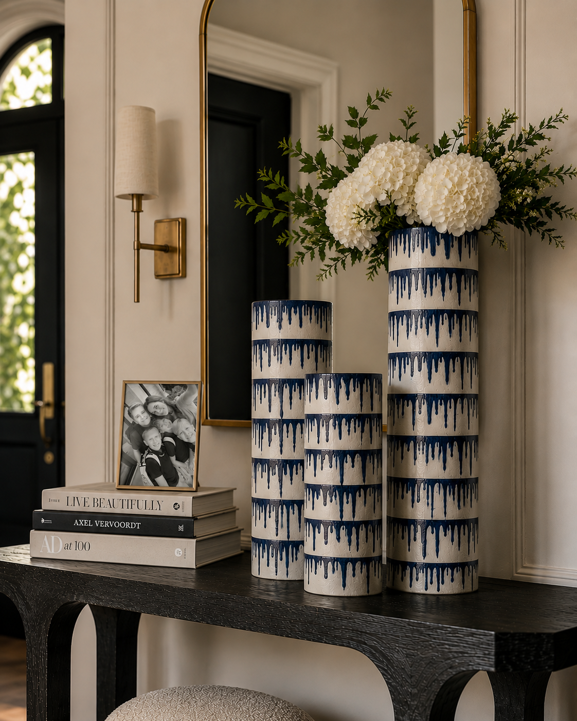 Three tall vases with blue drip patterns, one with white flowers and greenery on a dark wooden table.