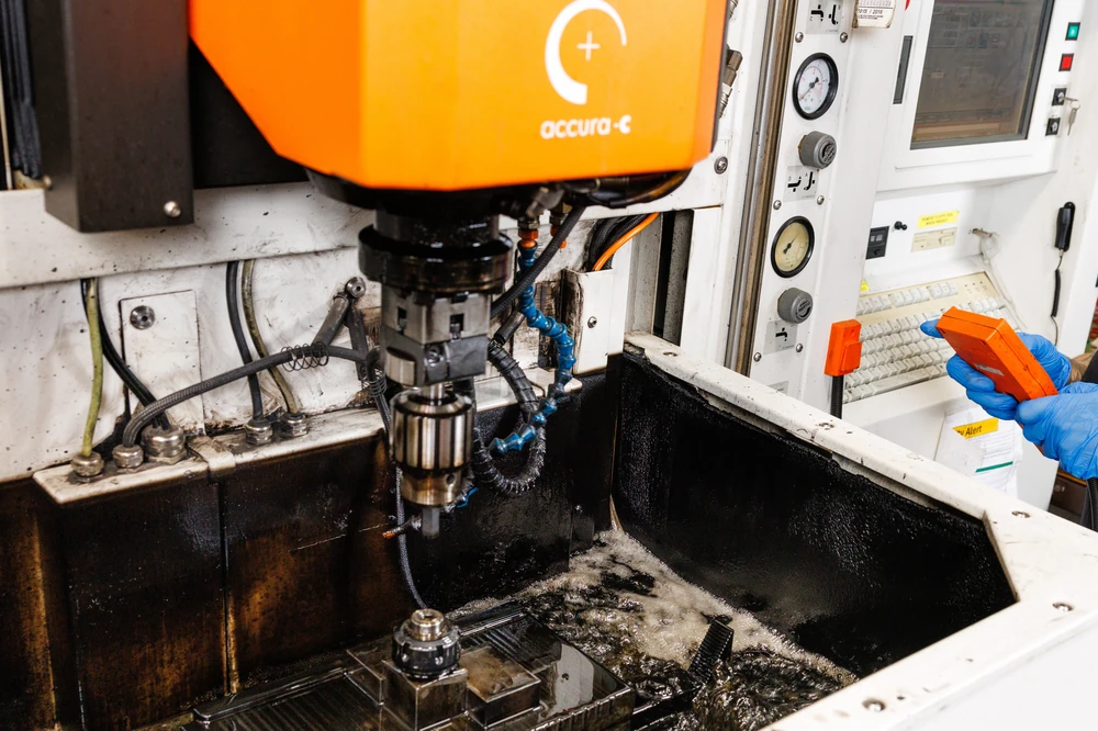 Sinker EDM electrode lowered into the dielectric tank while the operator holds the machine's remote