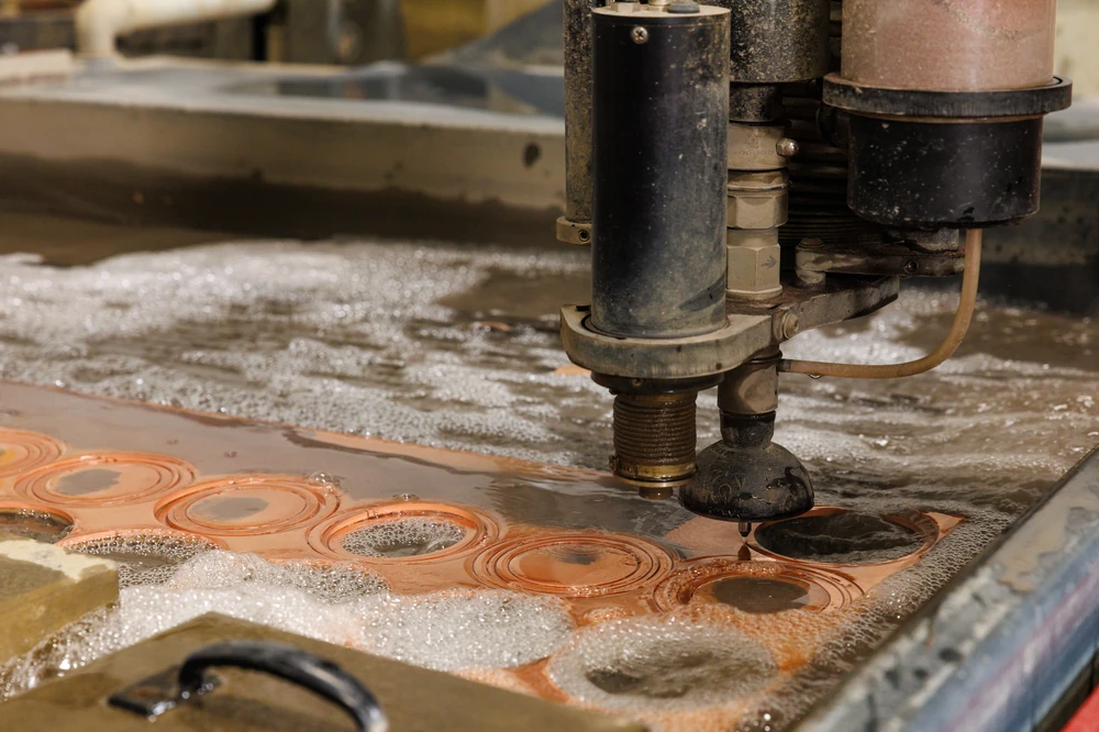 Waterjet nozzle cutting circular blanks from copper plate under water