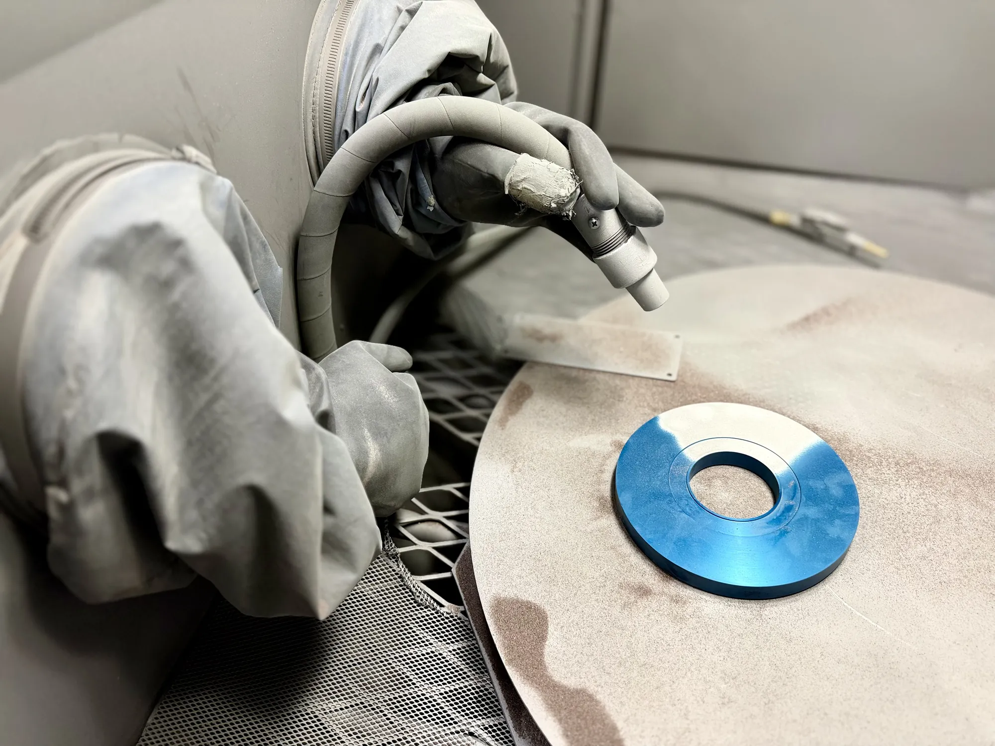 Operator in a dry blast cabinet preparing the surface of a blue machined ring
