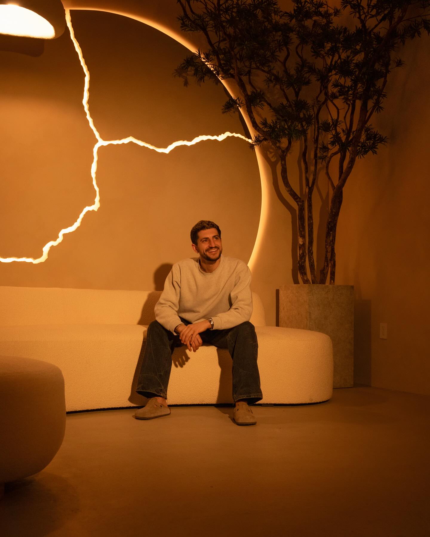 A man seated in a warm studio lounge beneath a glowing golden kintsugi arc at Kintsugi Yoga in Las Vegas