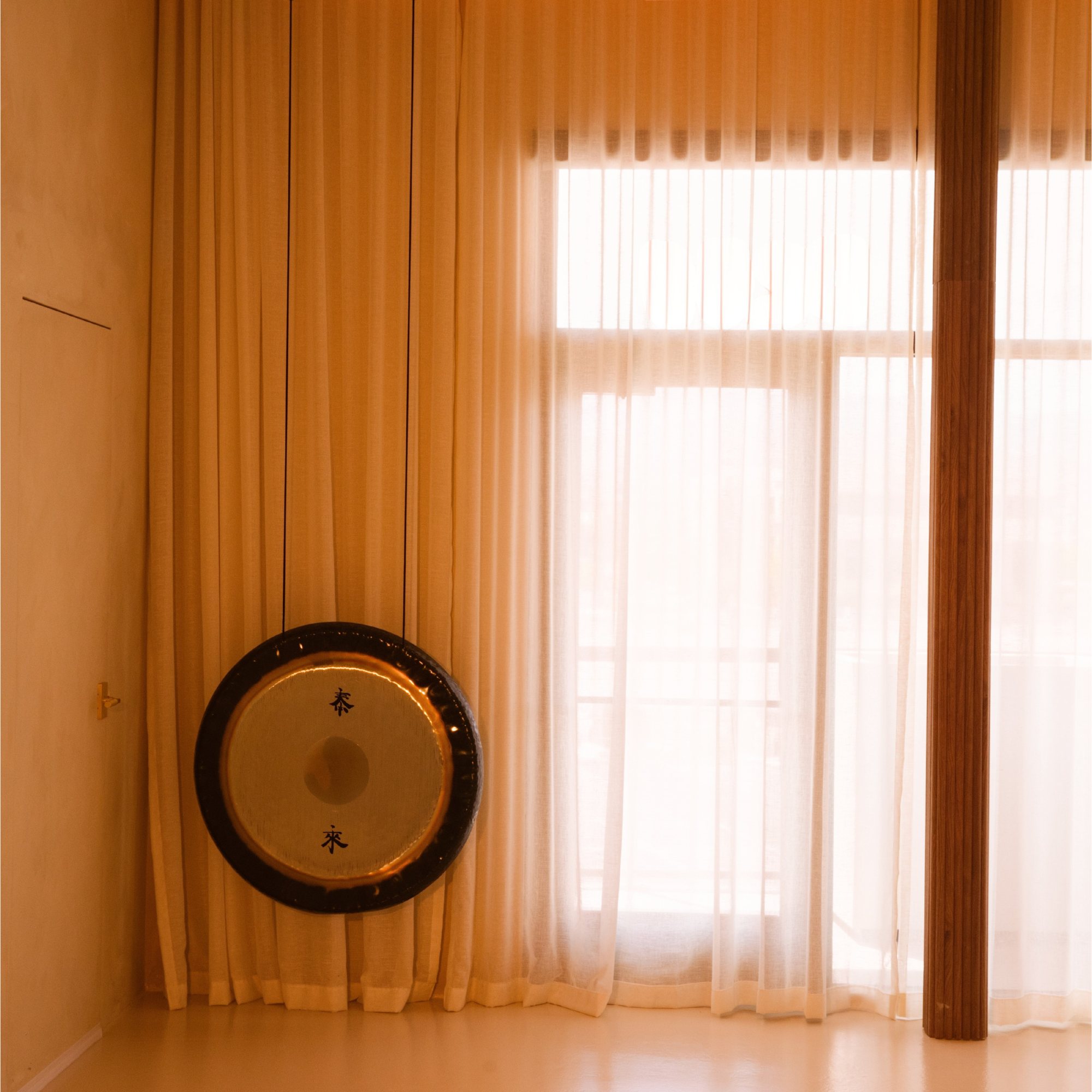 A ceremonial gong beside a sunlit, sheer-curtained window at Kintsugi Yoga in Las Vegas