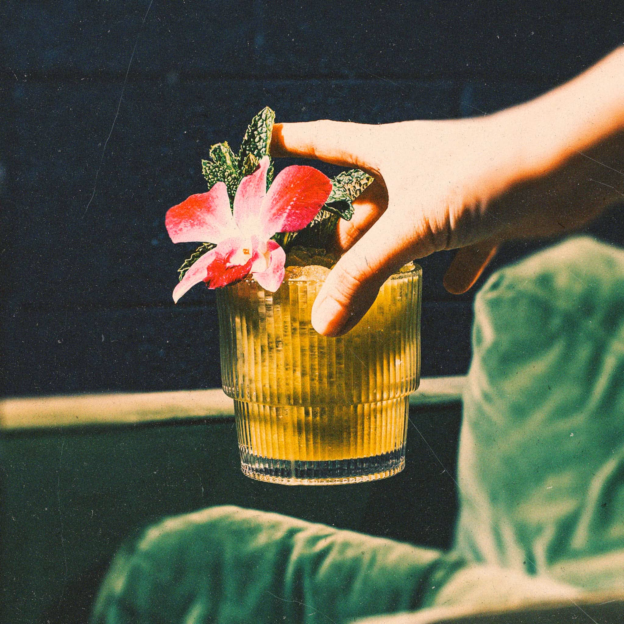 Hand holding a tropical cocktail garnished with mint and a pink orchid
