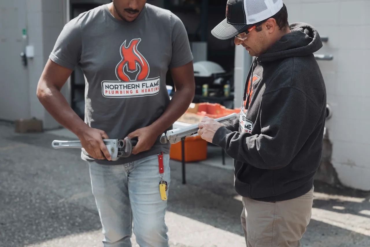 Two Northern Flame team members inspecting pipe wrenches outside the shop