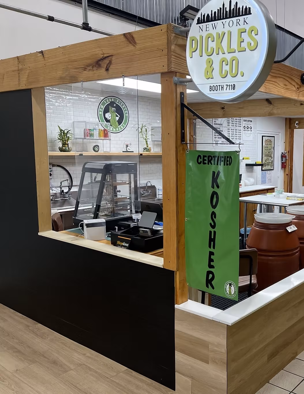 New York Pickles & Co. booth with certified kosher green banner and serving area inside market.